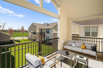 A balcony with a table and chairs overlooks a house and a lawn.